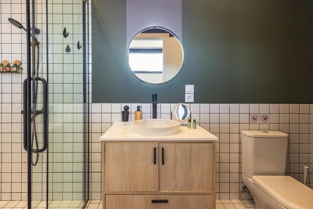 A modern bathroom with a glass shower enclosure, a round mirror, a sink with a round basin, and a toilet.