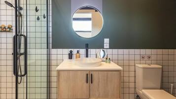 A modern bathroom with a glass shower enclosure, a round mirror, a sink with a round basin, and a toilet.