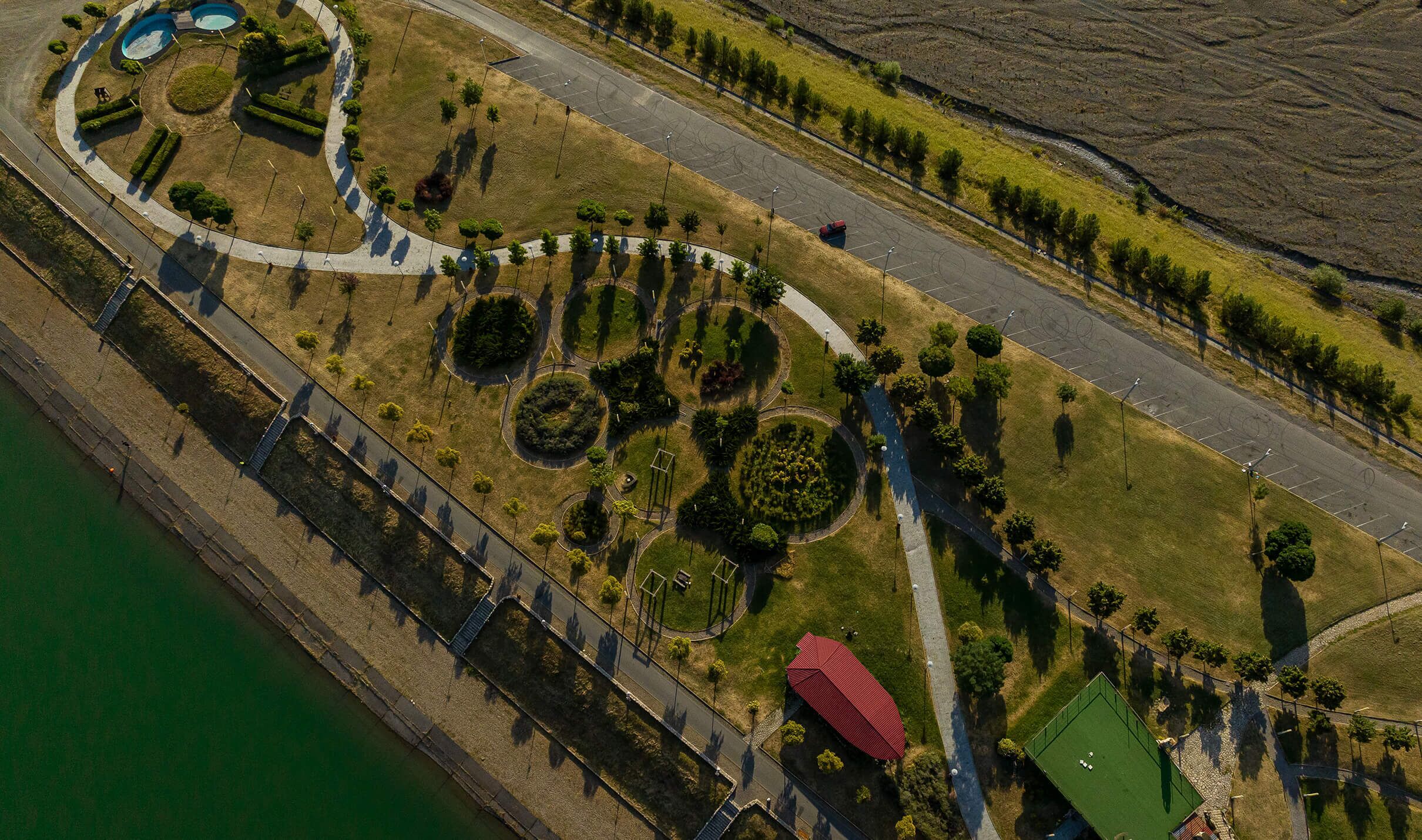 Luchtbeeld van een aangelegd gebied met paden, cirkelvormige tuinen en een waterpartij.