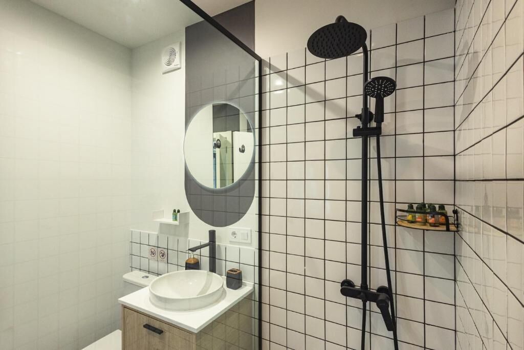 A modern bathroom with a white sink, a large mirror, and a black showerhead.