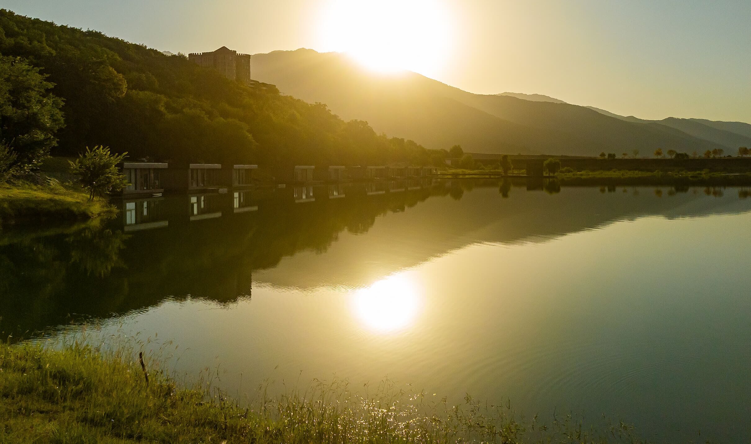 Une rivière paisible où se reflètent un château et des montagnes, sous un ciel dégagé.
