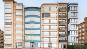 A multi-story residential building with a central curved facade, multiple balconies, and a uniform window pattern. - Cosy flat with frontal sea view (Koksijde)
