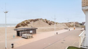 A beachside walkway with a wooden structure, possibly a kiosk or small shop, near the water. - Cosy flat with frontal sea view (Koksijde)