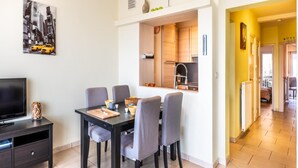 A modern apartment with a dining area, kitchen, and a TV on a dark wooden stand. - Cosy flat with frontal sea view (Koksijde)