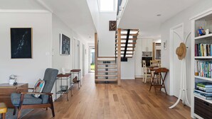A spacious living area with a wooden staircase, a bookshelf, and a dining area.