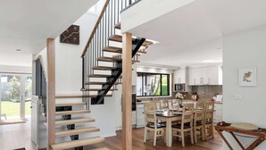 A modern kitchen with white cabinets, a dining area with wooden chairs, and a staircase with wooden steps and black railings.