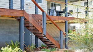 A modern outdoor staircase with a metal railing, leading to a covered area with a seating arrangement.