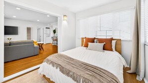 A modern hotel room with a large bed, a sofa, a small table, and a TV. - Downtown MB Gem: 2BR- 2 Blocks to the Ocean -Walk to Pier, Dining + Parking (Manhattan Beach)