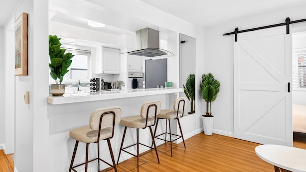 A modern kitchen with white cabinetry, a central island with bar stools, and a sliding barn-style door. - Downtown MB Gem: 2BR- 2 Blocks to the Ocean -Walk to Pier, Dining + Parking (Manhattan Beach)