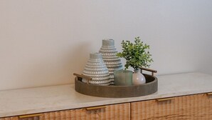 A wall-mounted painting of a beach scene, a wooden cabinet with a tray holding decorative items, and a small potted plant. - Downtown MB Gem: 2BR- 2 Blocks to the Ocean -Walk to Pier, Dining + Parking (Manhattan Beach)