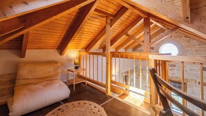 Une chambre confortable située dans les combles, avec des poutres apparentes, un lit confortable, une petite table avec une lampe et une vue par la fenêtre.