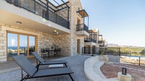 Une maison moderne à plusieurs niveaux, dotée d’une façade en pierre, d’un espace extérieur aménagé et offrant une vue sur la mer.