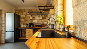 A modern kitchen with a stone wall, wooden countertop, stainless steel appliances, and a black sink. - Villa Seiri – Vacation villa in Crete (Gavalochori)