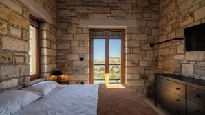 A bedroom with stone walls, a bed, a dresser, and a window with a view of the countryside. - Villa Seiri – Vacation villa in Crete (Gavalochori)