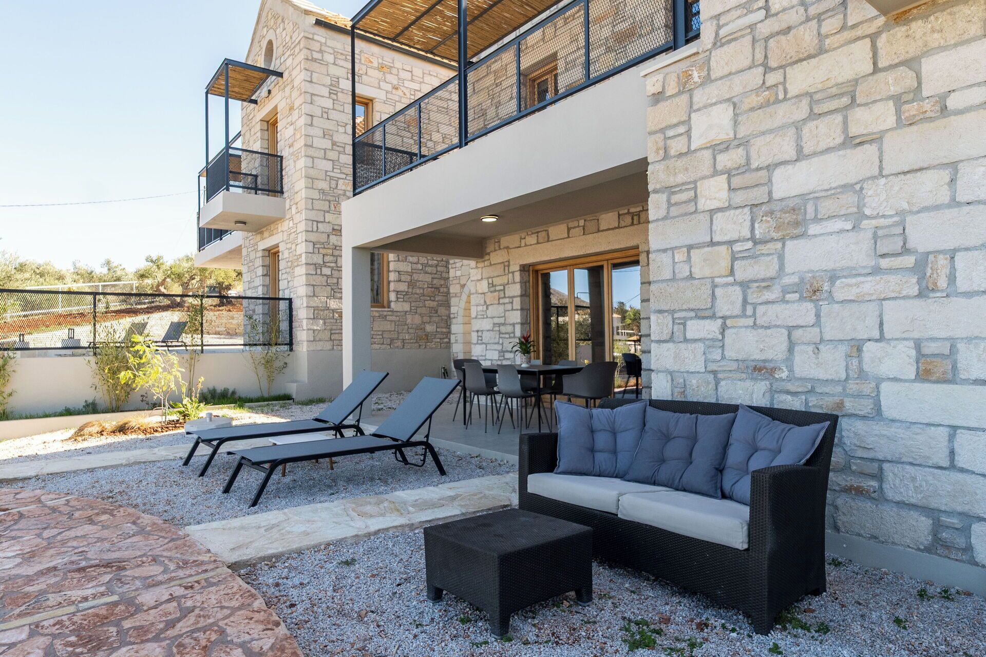 A modern outdoor seating area with a stone wall, a sofa, and lounge chairs.