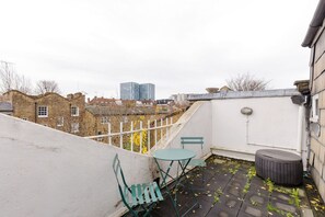 A rooftop terrace with a white wall, a green bench, a small table, and a trash bin. - Spacious 4BDR Home by Kings Cross Station (Greater London)