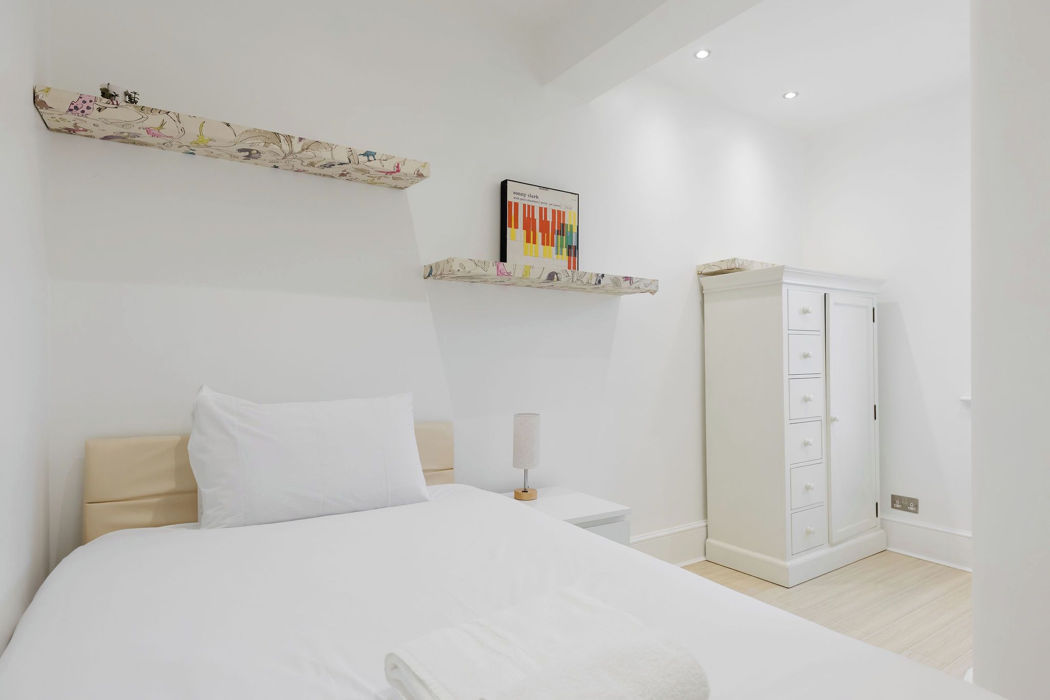 A bedroom with a bed, a wardrobe, and a shelf with a book.