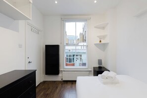 A hotel room with a bed, a dresser, a window with a view of buildings, and a radiator. - Spacious 4BDR Home by Kings Cross Station (Greater London)