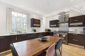 A modern kitchen with dark cabinetry, a wooden dining table, and a large window. - Spacious 4BDR Home by Kings Cross Station (Greater London)