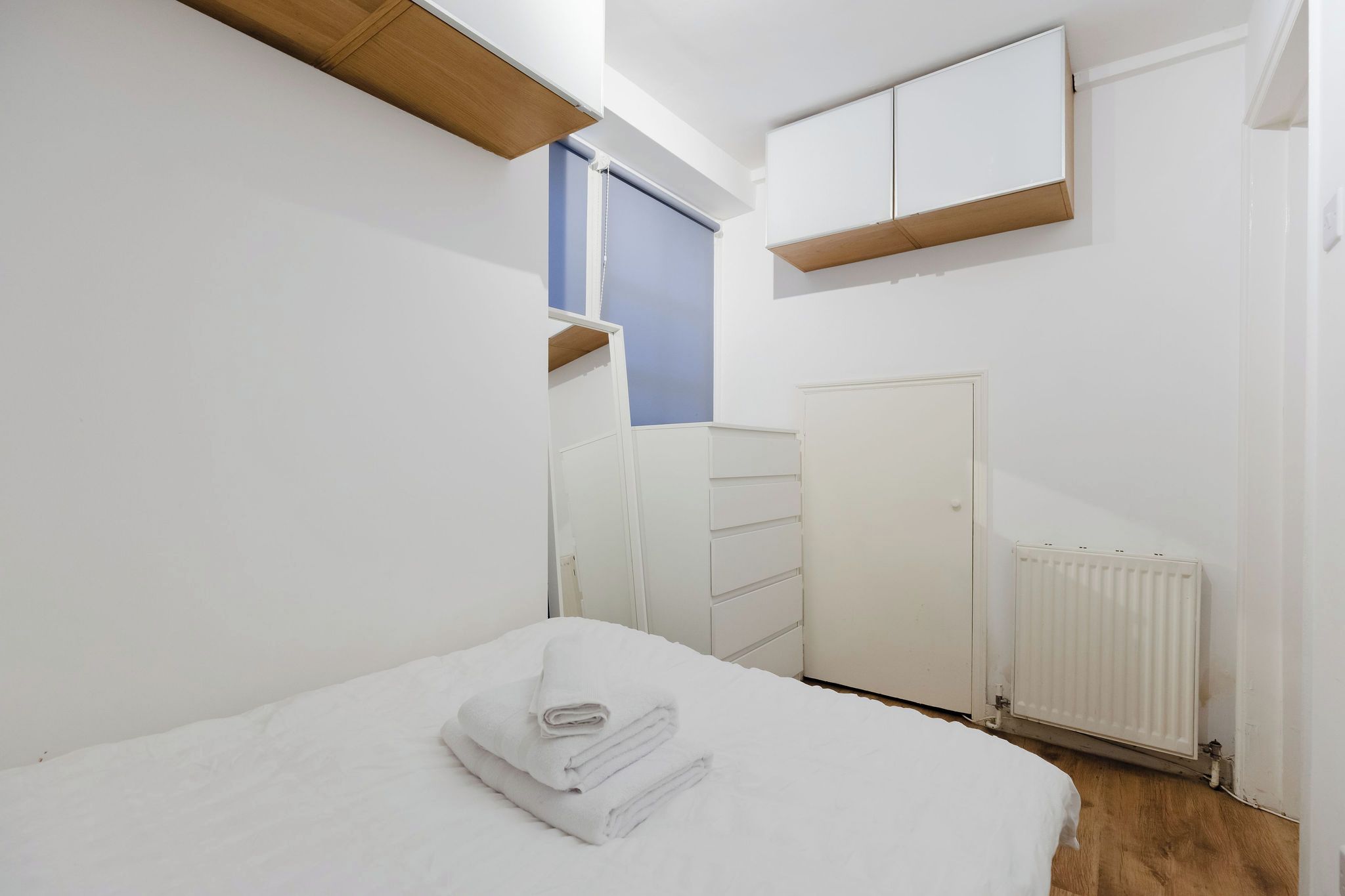 Un dormitorio con cama, cómoda, radiador y ventana con persiana.