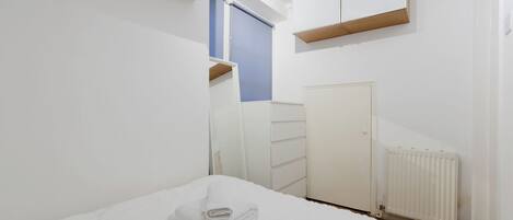 A bedroom with a bed, a dresser, a radiator, and a window with a blind.
