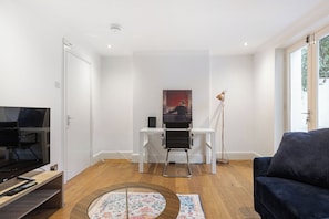 A modern living room with a flat-screen TV, a black sofa, a coffee table, a painting on the wall, and a floor lamp. - Spacious 4BDR Home by Kings Cross Station (Greater London)