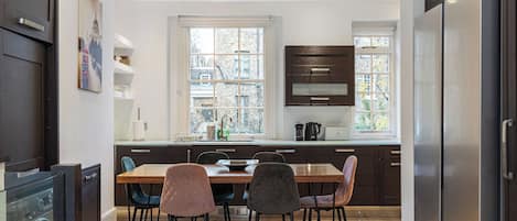 A modern kitchen with a dining table, chairs, and a refrigerator.