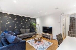 Ein modernes Wohnzimmer mit einem grauen Sofa, einem Couchtisch, einem Fernseher und einer Treppe.
