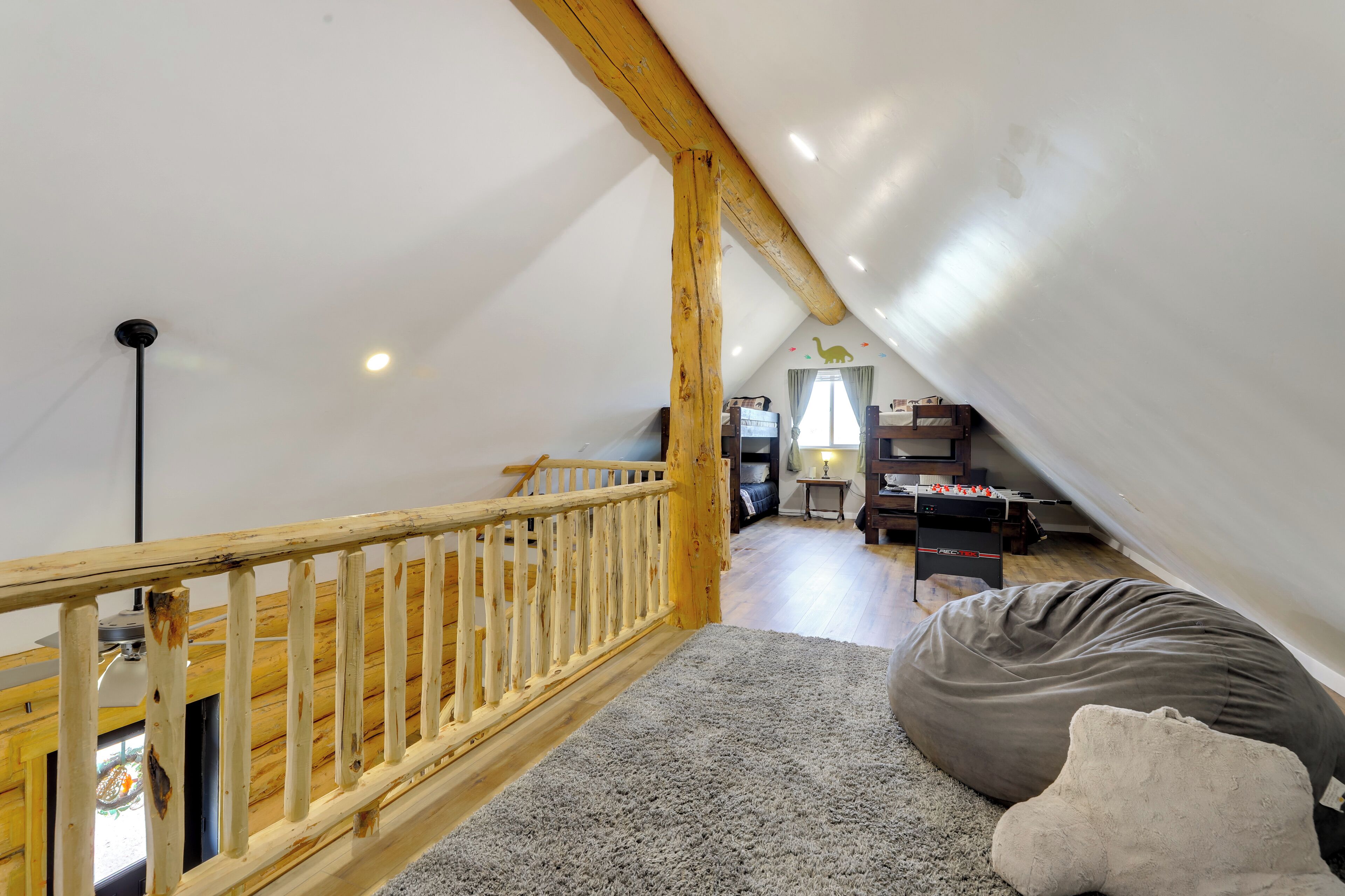 A loft bedroom with a wooden railing, a gray carpet, and a gray bean bag.