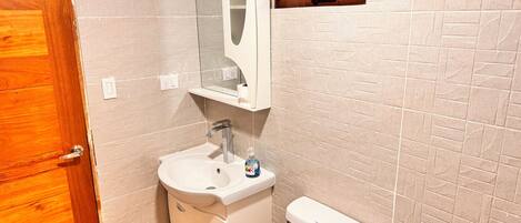 A bathroom with a wooden door, a white sink with a mirror above it, a toilet, and a window with a towel rack.