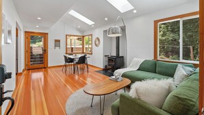 Una sala de estar moderna con un sofá verde, piso de madera, un comedor con sillas, una chimenea y tragaluces.