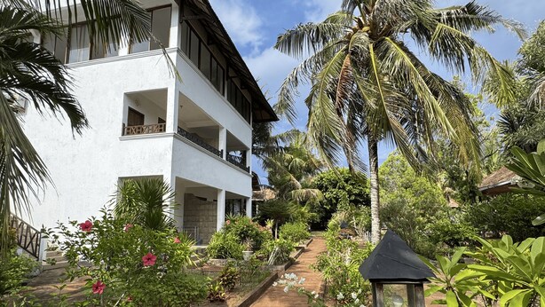 A two-story building with a balcony, surrounded by lush greenery and a pathway leading to a wooden structure. - Hotel Patma Bira (Bira)
