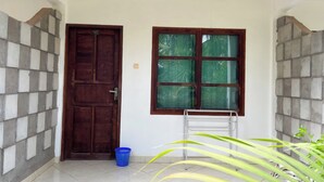 A room with a wooden door, a window with a view of greenery, a blue plastic basket, and a metal chair. - Hotel Patma Bira (Bira)