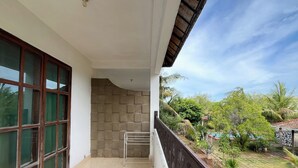 A balcony with a tiled floor, a metal railing, and a view of a garden with various plants and a pool. - Hotel Patma Bira (Bira)