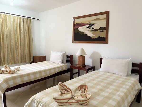 A hotel room with two beds, a painting on the wall, a lamp, and a window with curtains. - Hotel Patma Bira (Bira)