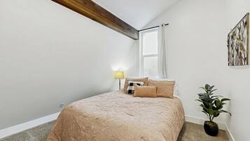 Een slaapkamer met een groot bed, een nachtkastje, een lamp, een raam en een plant.