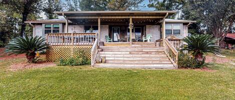 A two-story house with a wooden deck, a front porch, and a small outdoor seating area.