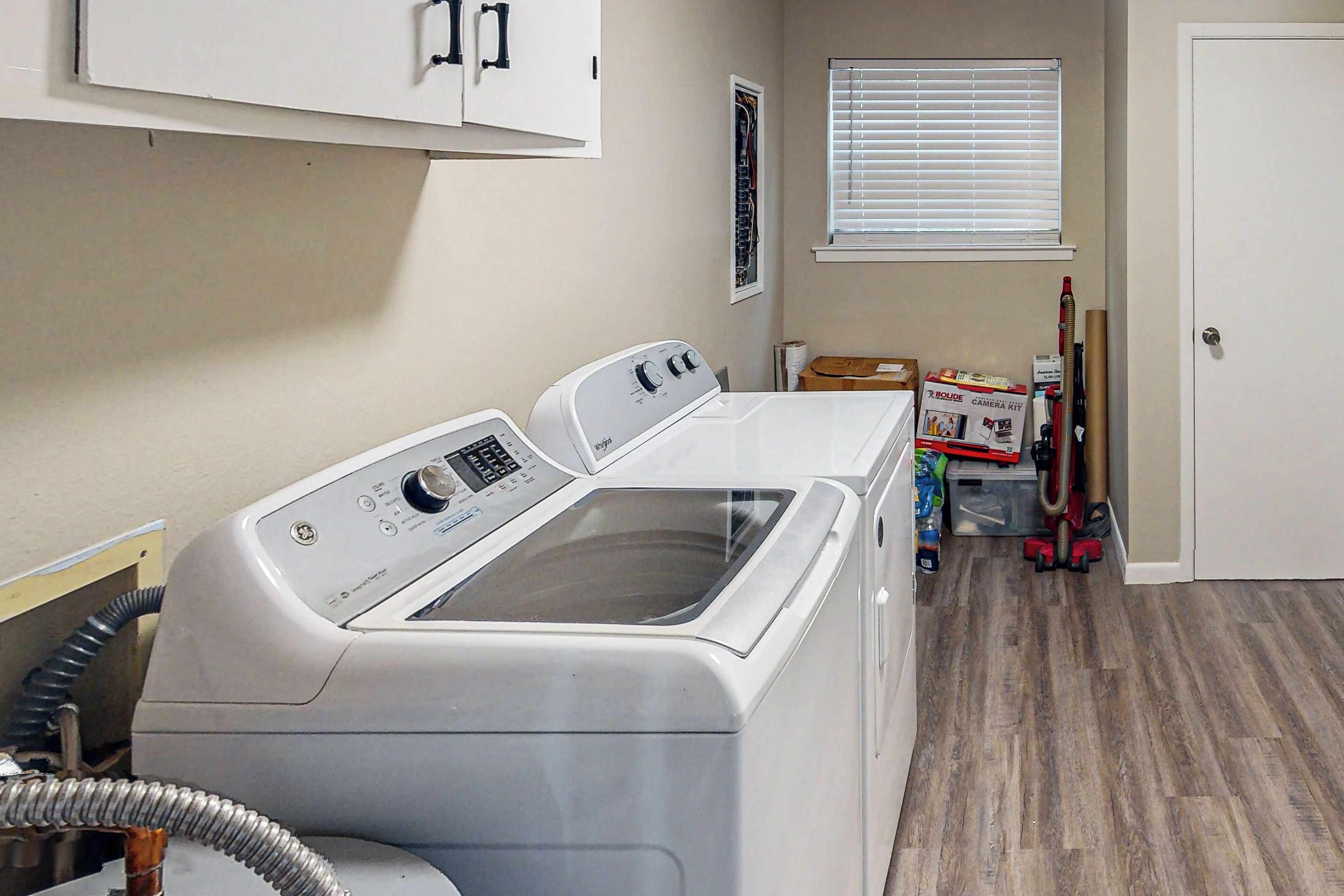 A laundry room with a front-loading washer and dryer, a window with blinds, and a door.