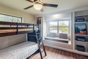 Ein Stockbett mit Fensterbank, Deckenventilator und Bücherregal mit beschrifteten Boxen.