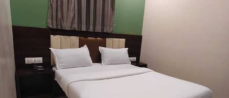 Uma cama bem arrumada em um quarto com paredes verdes, cabeceira de madeira e mesa de cabeceira com uma luminária.