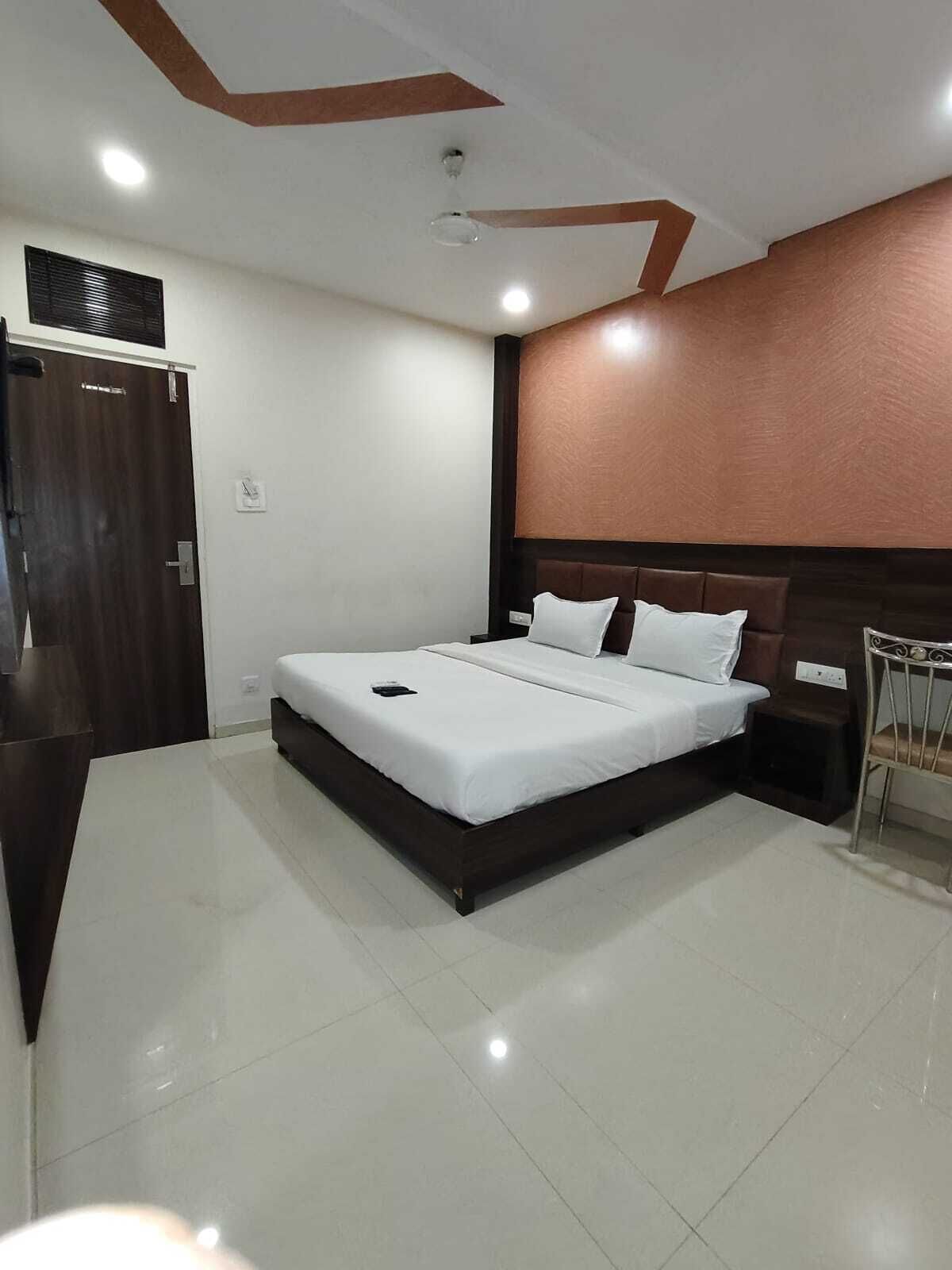 A modern hotel room with a large bed, a wooden headboard, a small bedside table, and a chair.
