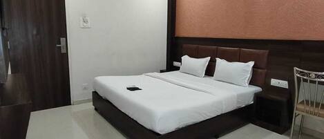 A modern hotel room with a large bed, a wooden headboard, a small bedside table, and a chair.