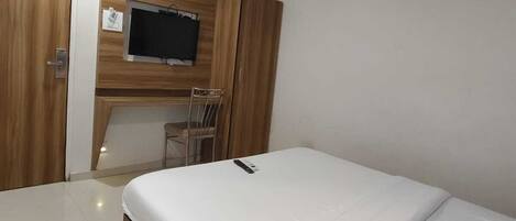 A bedroom with a bed, a TV mounted on the wall, a ceiling fan, and a wooden wardrobe.