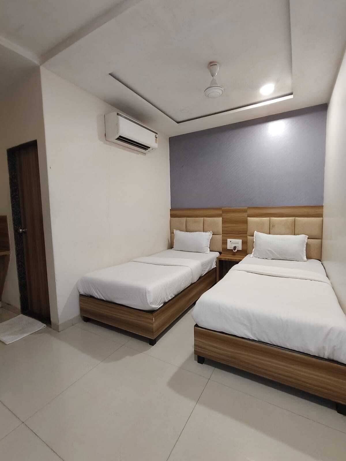 A hotel room with two single beds, a ceiling fan, an air conditioning unit, and a wooden headboard.