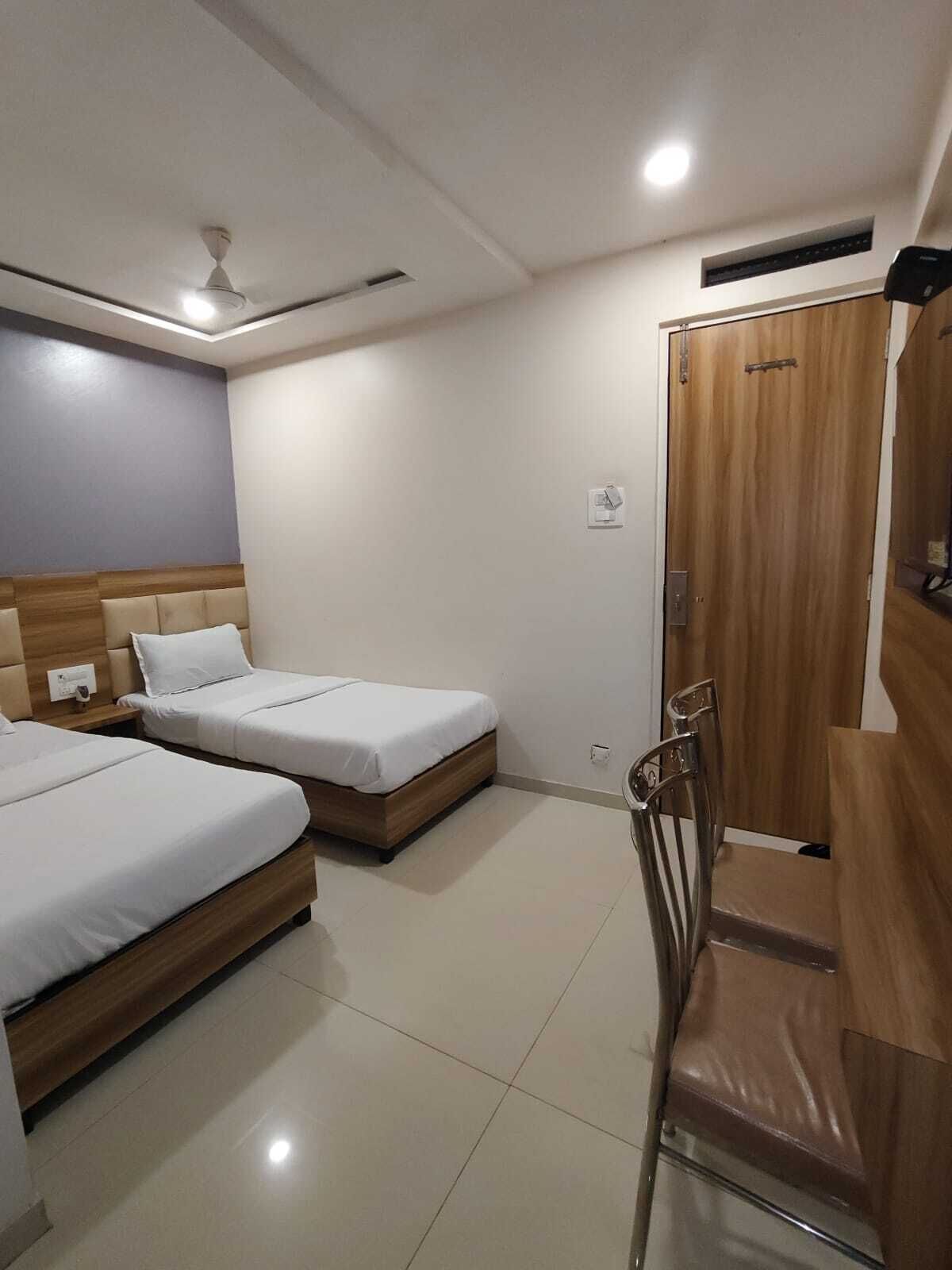 A hotel room with two single beds, a wooden wardrobe, a chair, and a ceiling fan.