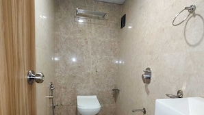 A small, tiled bathroom with a toilet, a shower, and a sink. - HOTEL BKC NX Rooms (Mumbai)