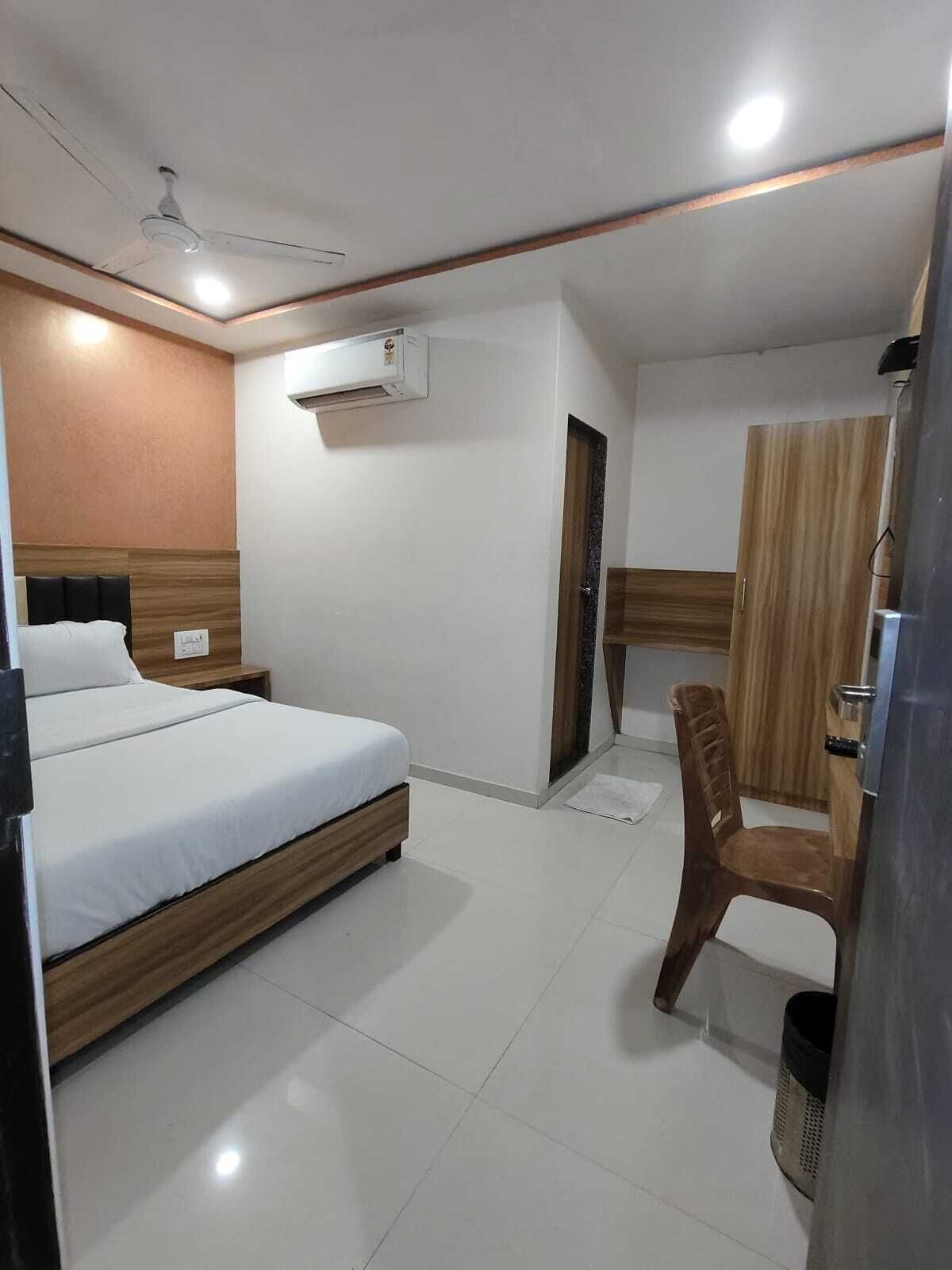 A hotel room with a bed, a chair, a wardrobe, and an air conditioning unit.