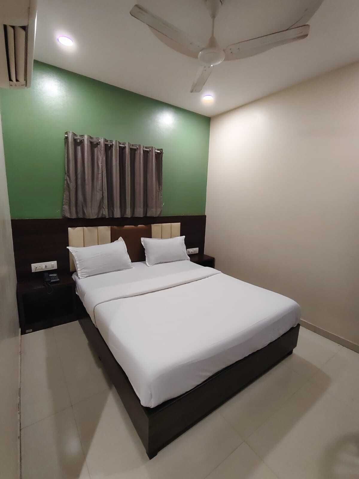 A neatly made bed in a room with green walls, a ceiling fan, and a nightstand with a lamp.