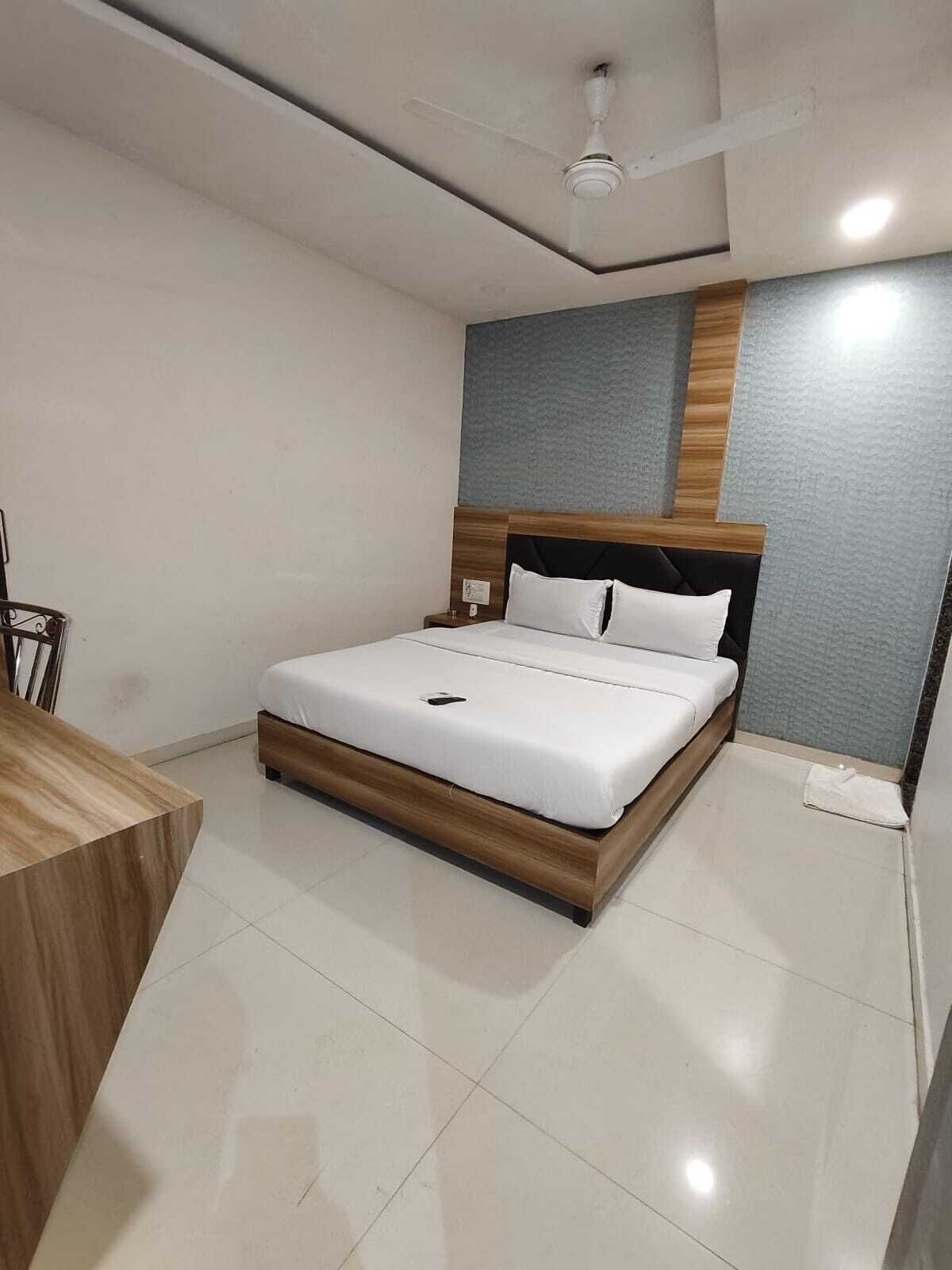 A modern bedroom with a wooden bed frame, white bedding, a desk, and a ceiling fan.