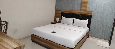 A modern bedroom with a wooden bed frame, white bedding, a desk, and a ceiling fan.